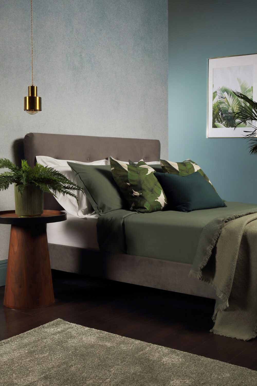 Blue and grey bedroom with tropical print, hanging gold lamp and wooden bedside table