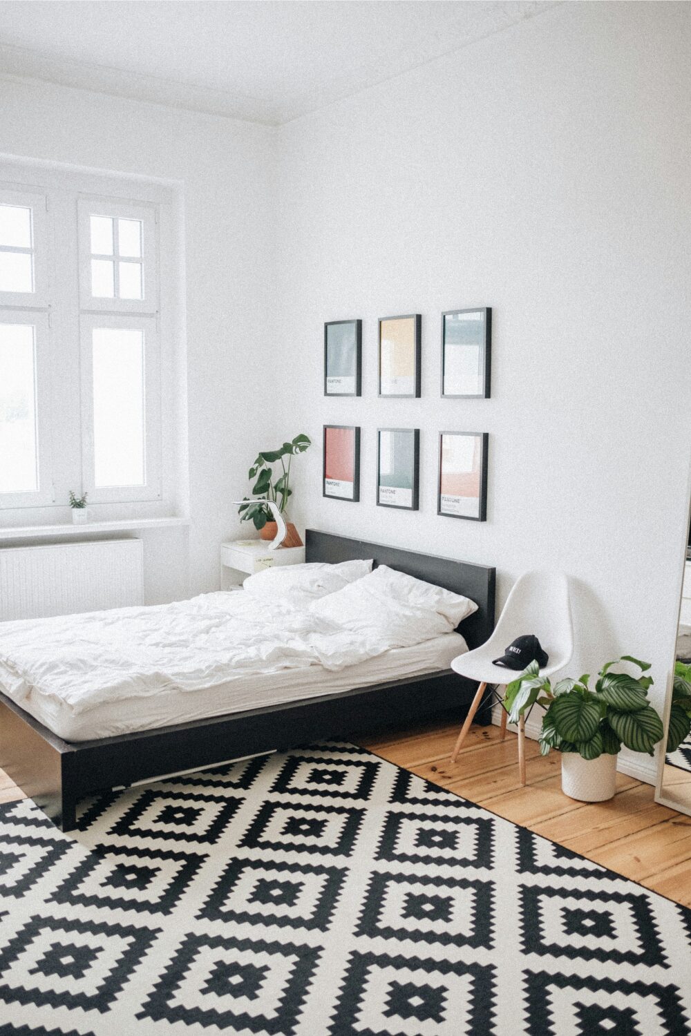 White bedroom with framed colour prints, wood floor, black and white patterned rug