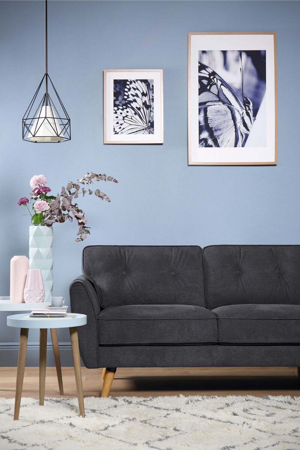 Grey sofa in blue living room next to blue side tables holding pastel vases