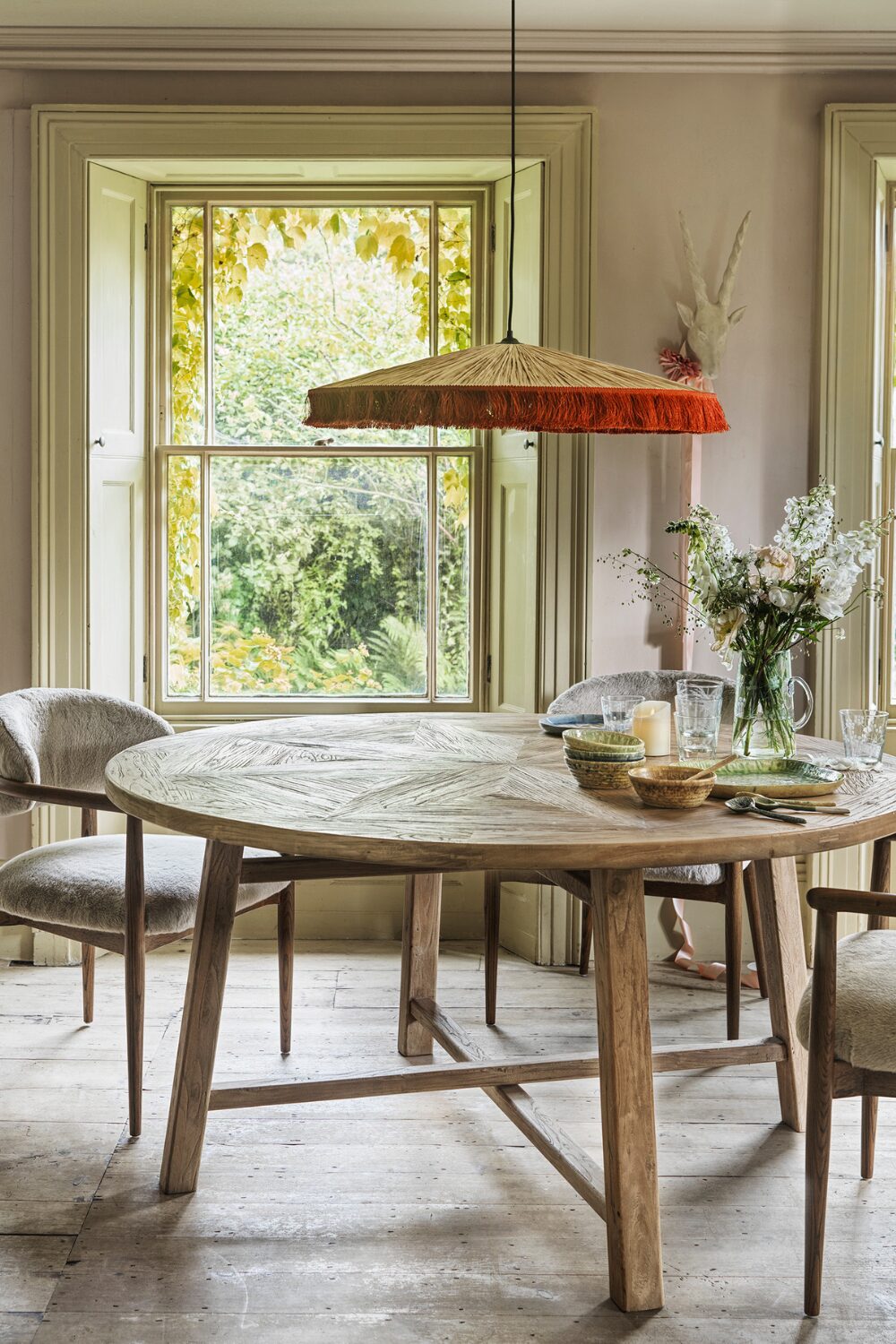Round wooden dining table with white chairs under an orange hanging lamp