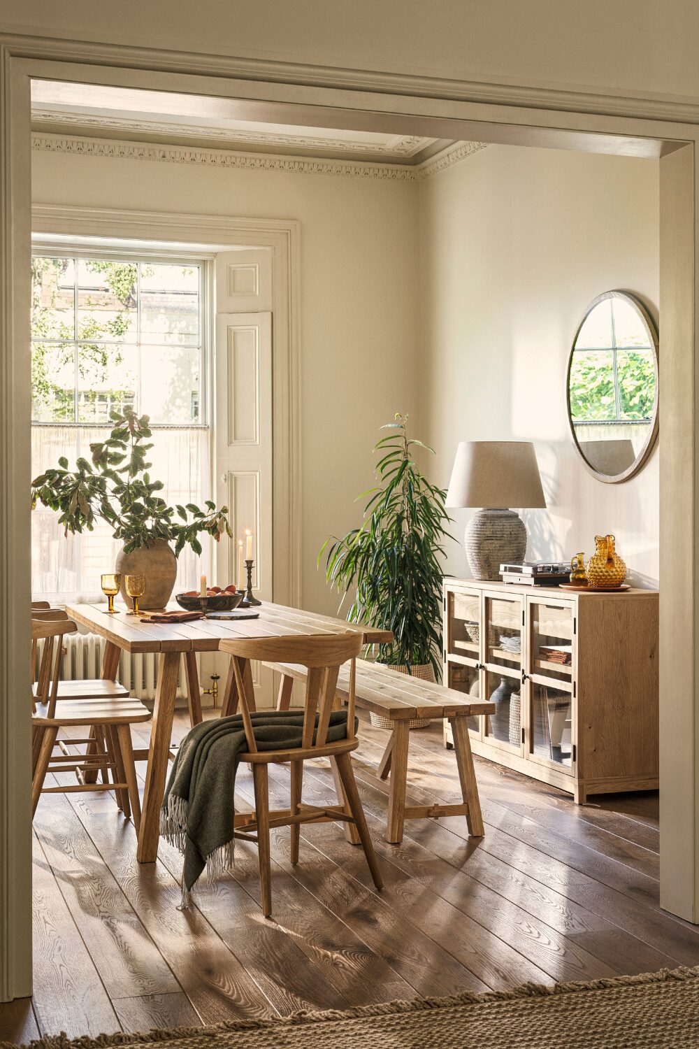 Wooden dining table and chairs next to wooden sideboard and round mirror