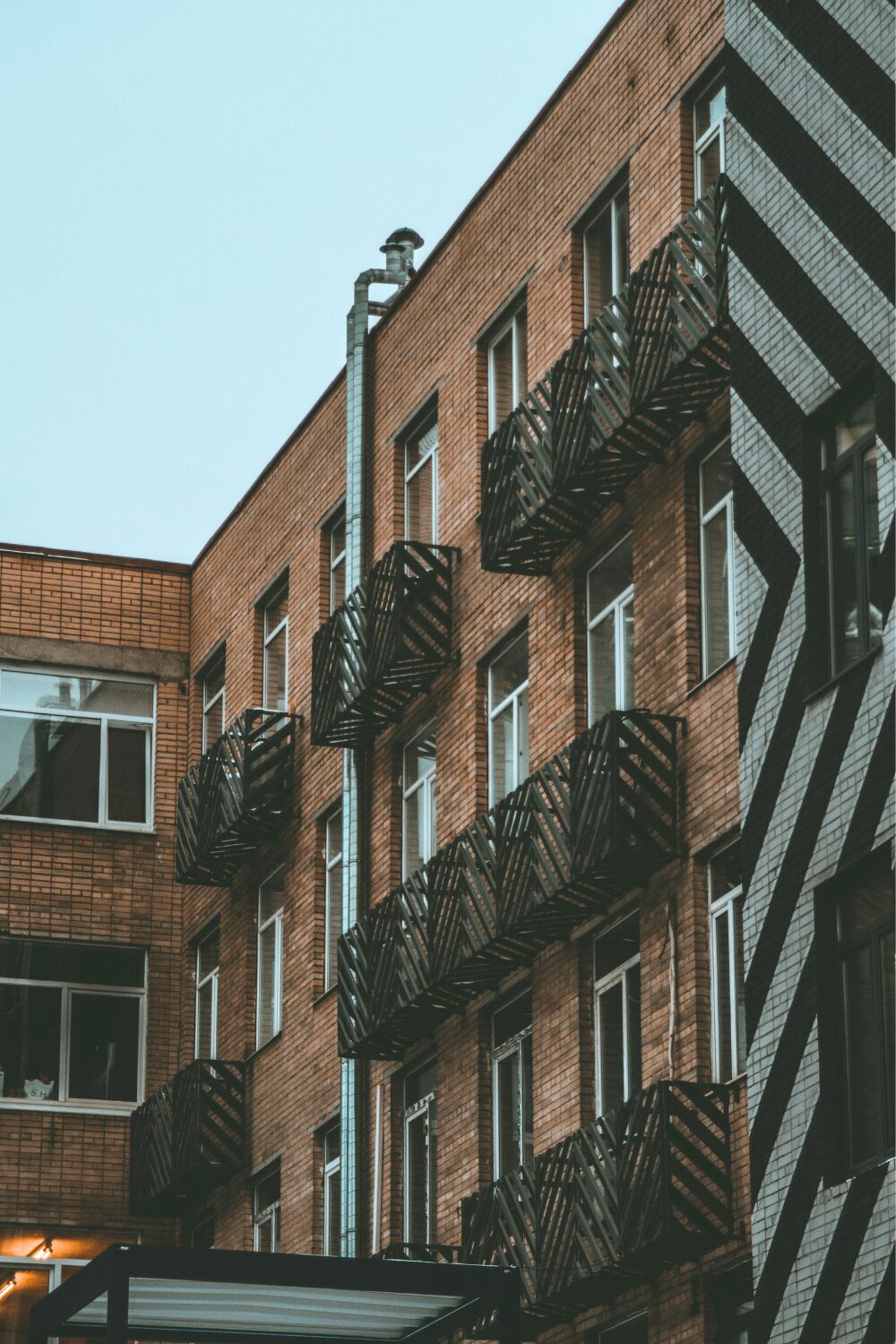 Exterior of red brick building with black metal balconies, and black & white striped wall