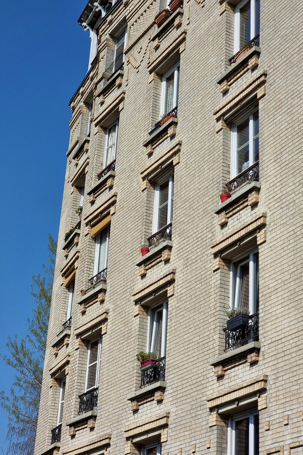 Exterior of yellow brick building with many windows and black metal Juliet balconies