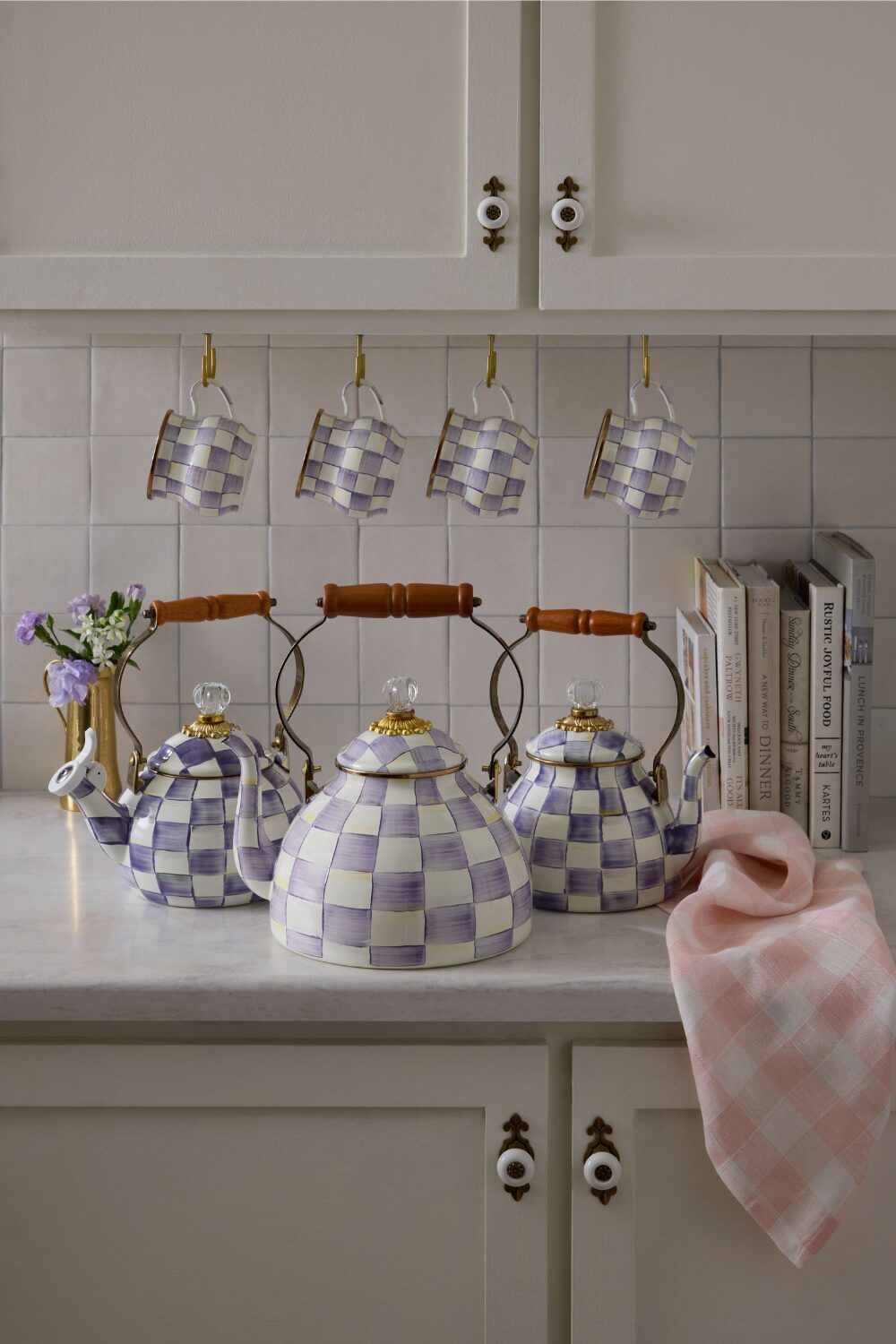 Three chequered kettles on white kitchen counter under row of hanging mugs