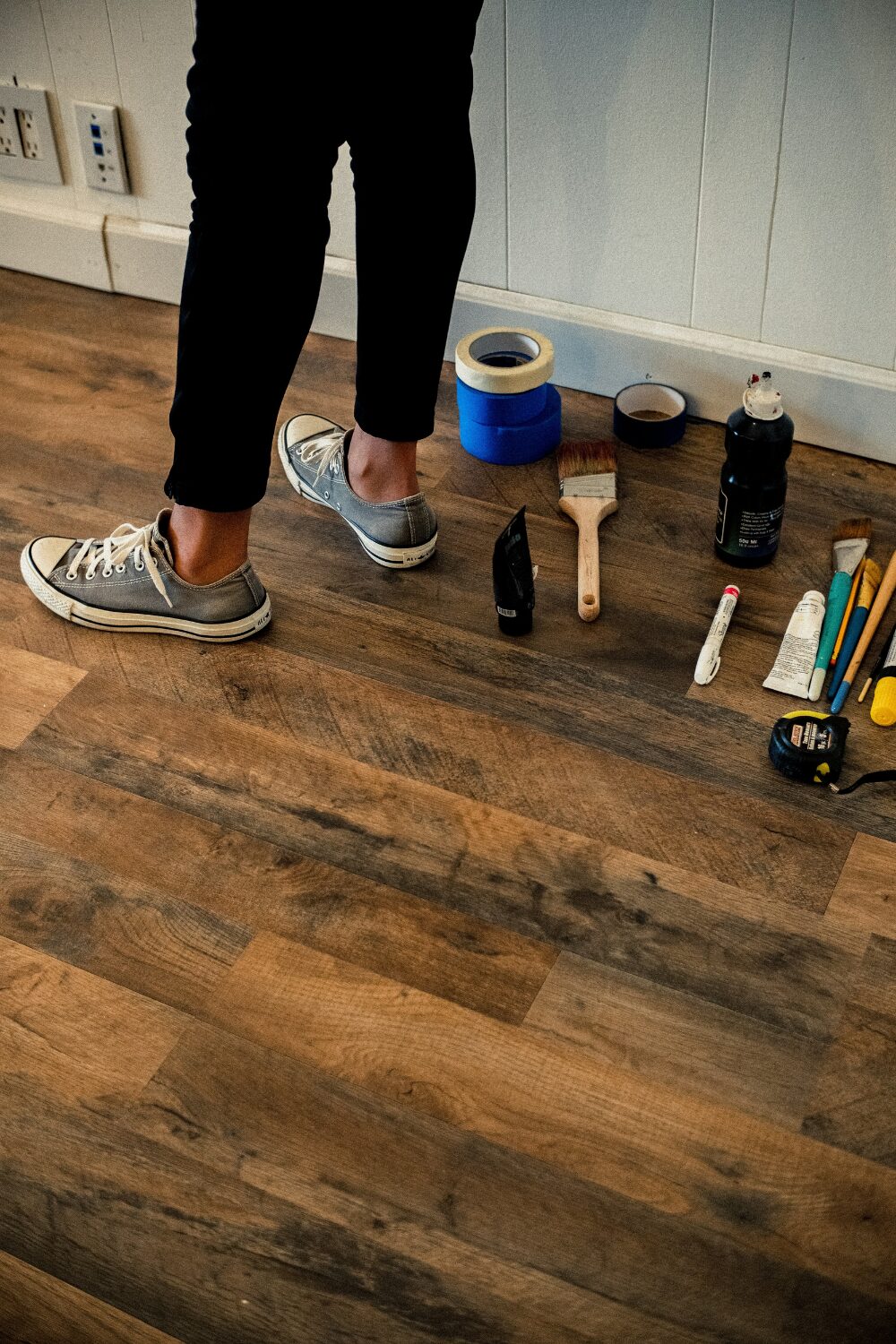 Person stands on wood floor next to row of paint supplies