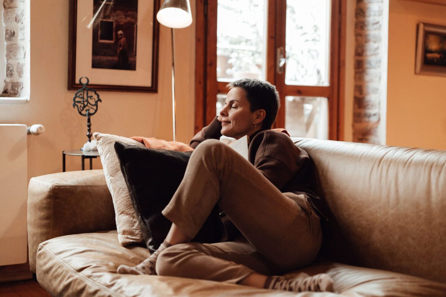 Woman sitting on brown sofa in orange living room with eyes closed