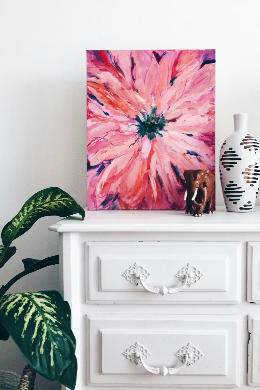 White chest of drawers with pink flower canvas and white vase resting on top
