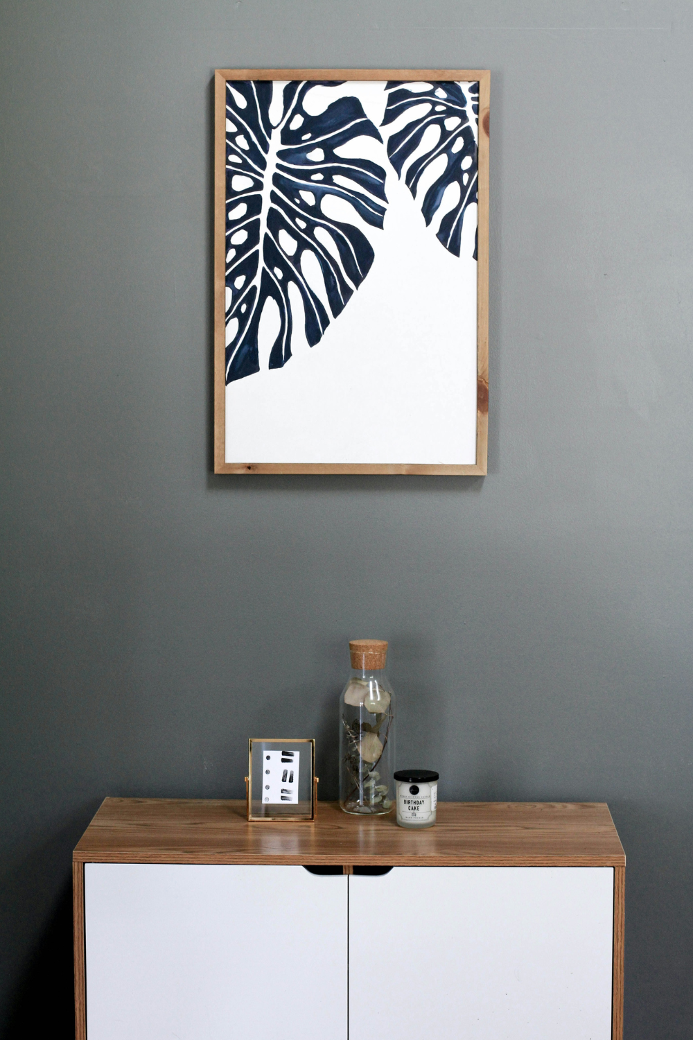 Framed black & white botanical print on grey wall above wooden cabinet