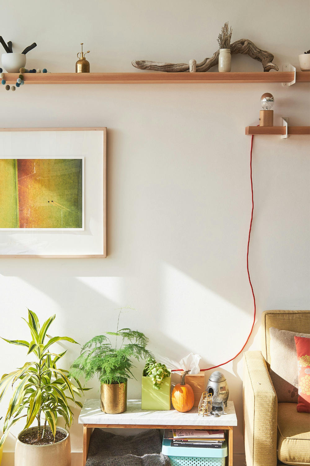 Floating wooden shelves above a framed green print, white table holding vases, and plant pot