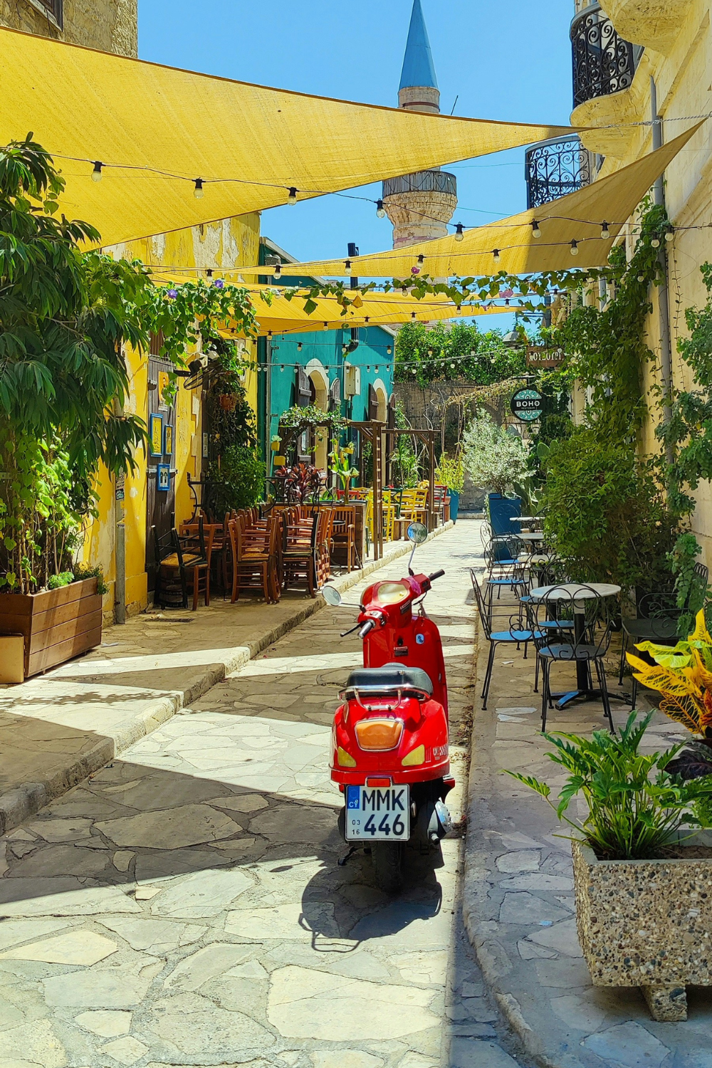 Stone street of bright yellow and blue cafes with red scooter and yellow shades strung above