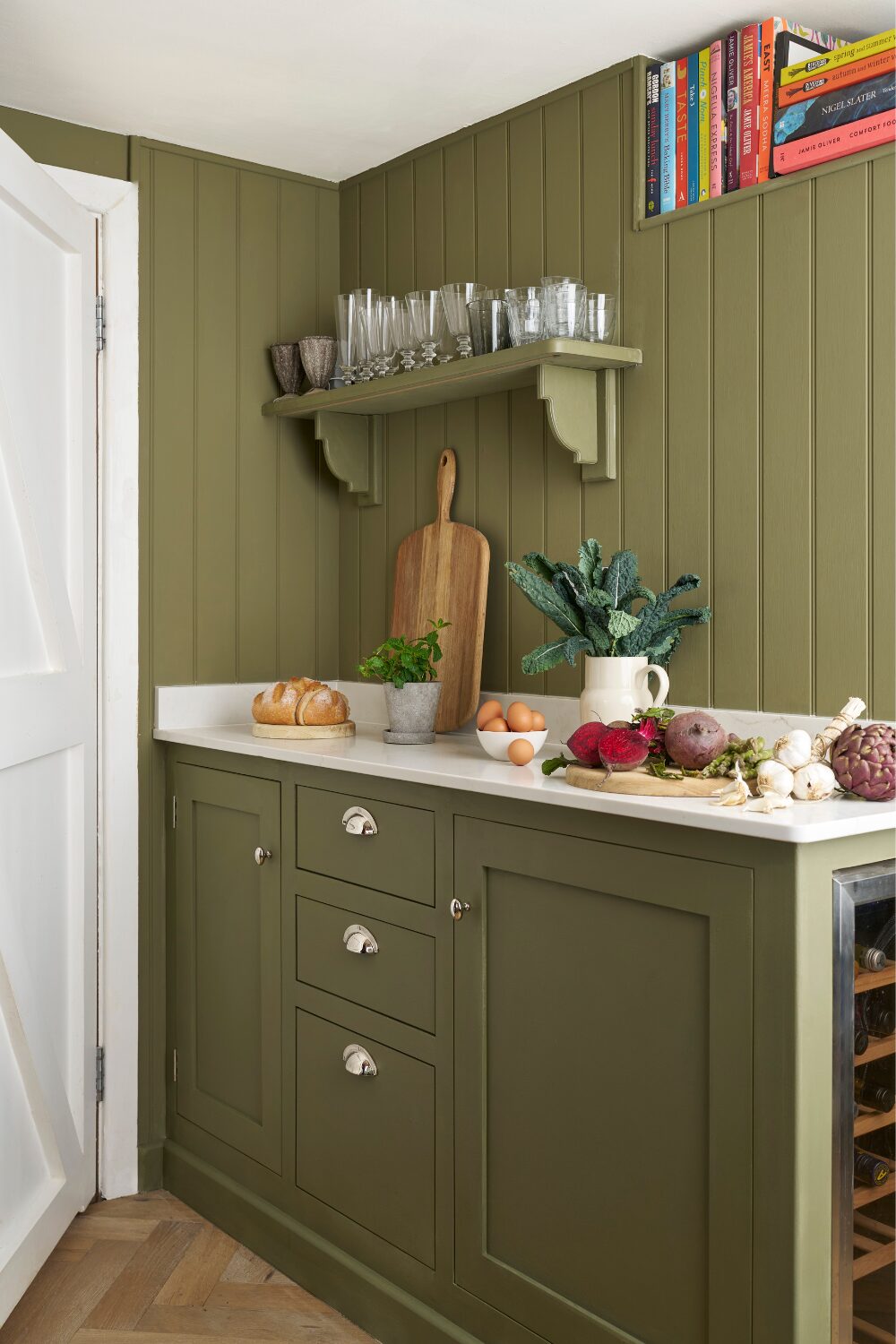 Olive green kitchen cabinets and wooden slat wall with shelf holding glasses