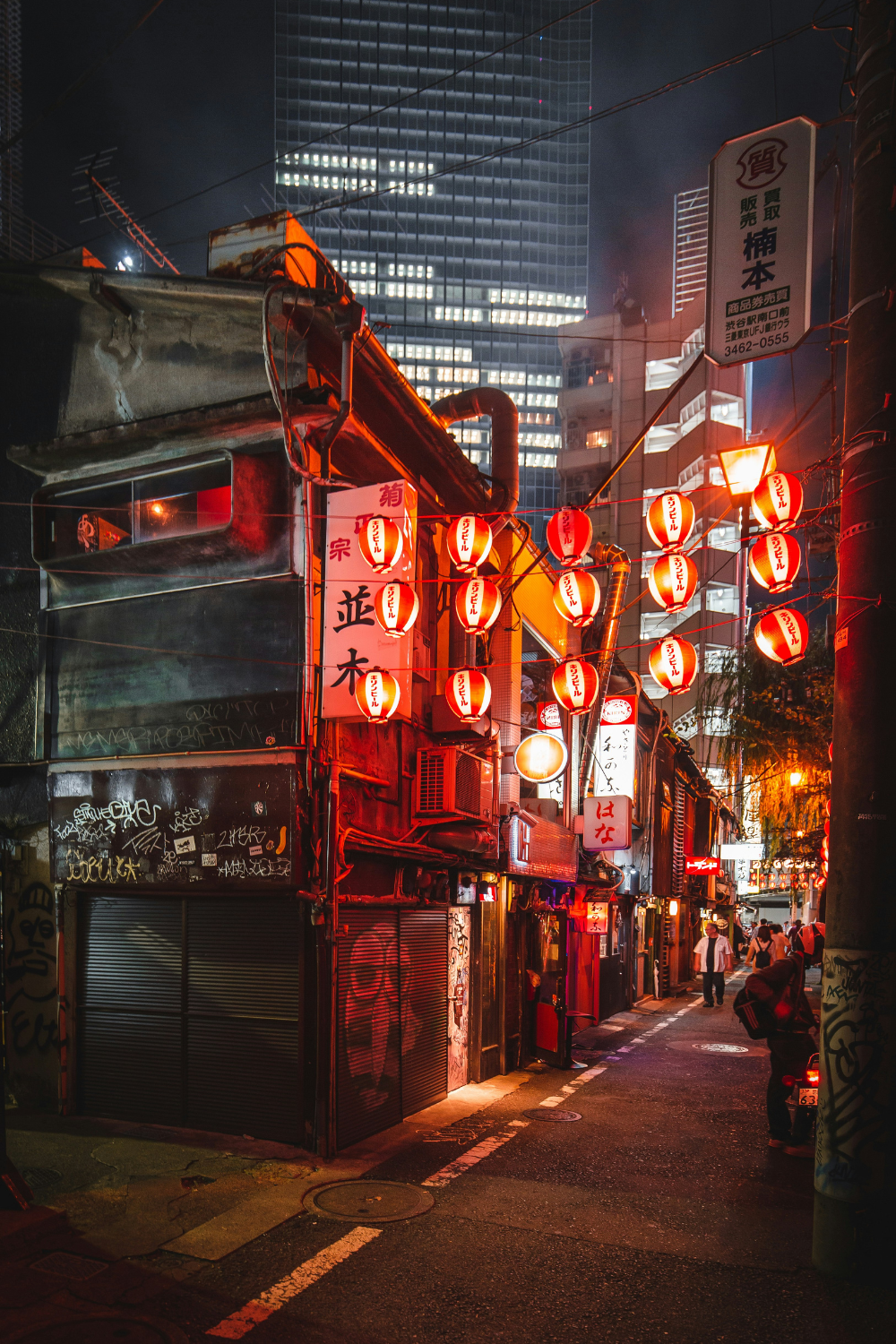 Tokyo street at night lit by rows of red lanterns and neon signs with skyscraper beyond