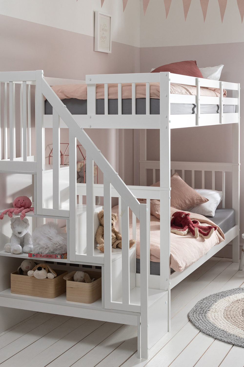 White bunk bed with stair storage holding soft toys in light pink room