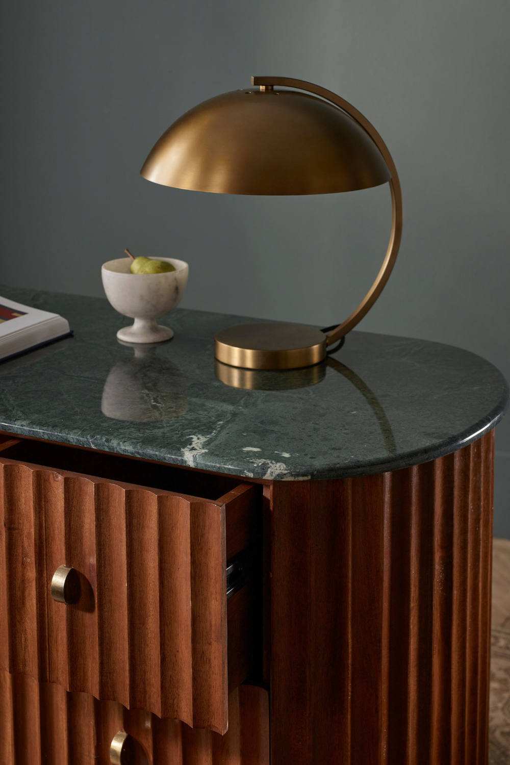 Curved gold lamp on dark marble-topped desk with fluted wooden base