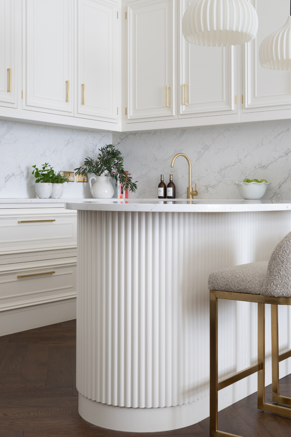 White kitchen with fluted island, padded barstools and gold tap