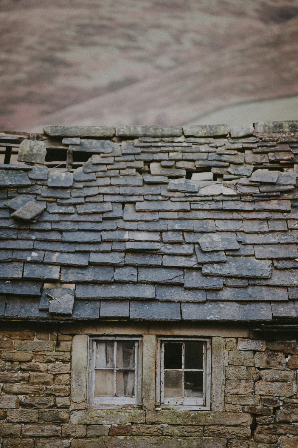 Dilapidated brick cottage with holey slate tiled roof