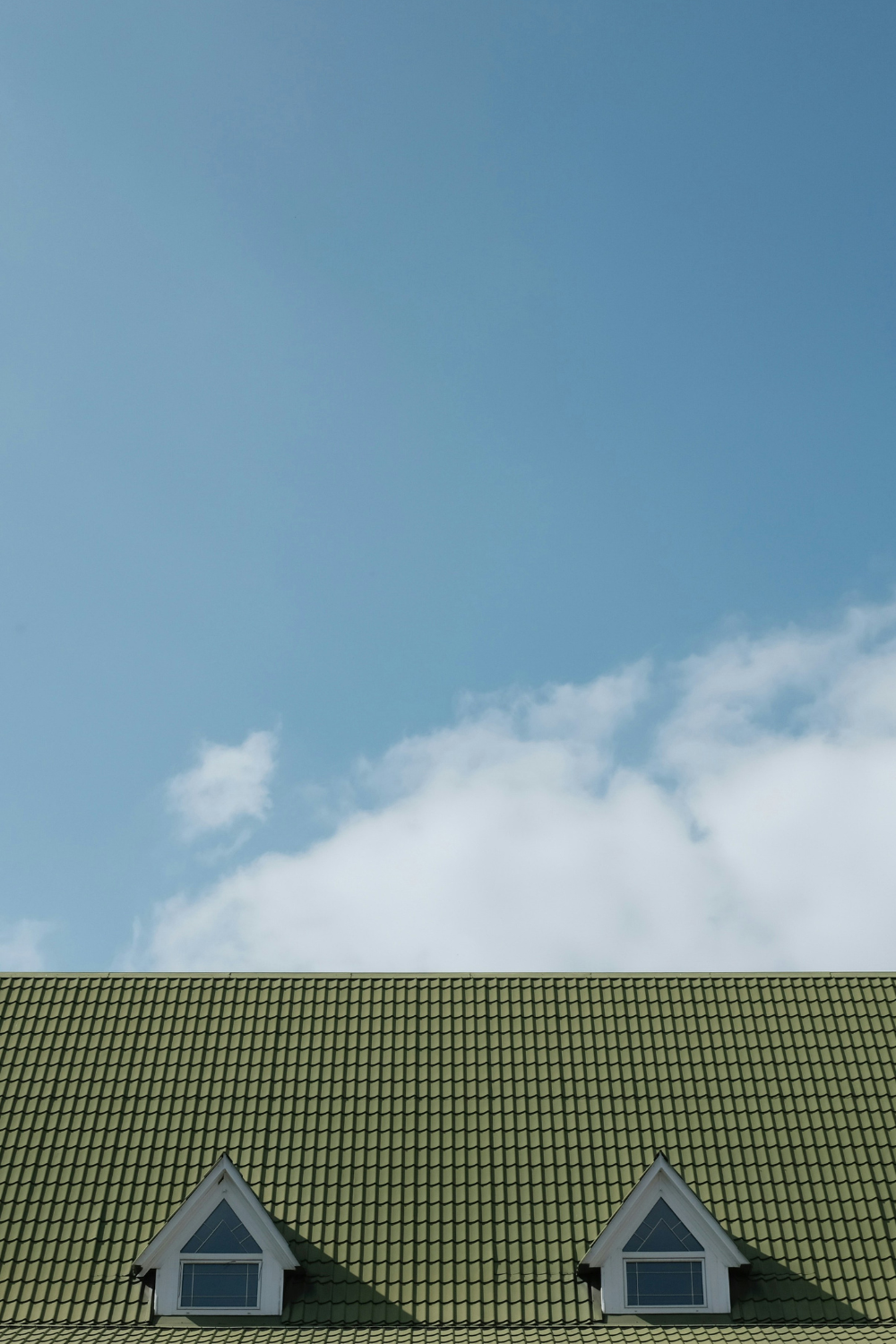 Green tiled roof with two inset windows next to blue sky