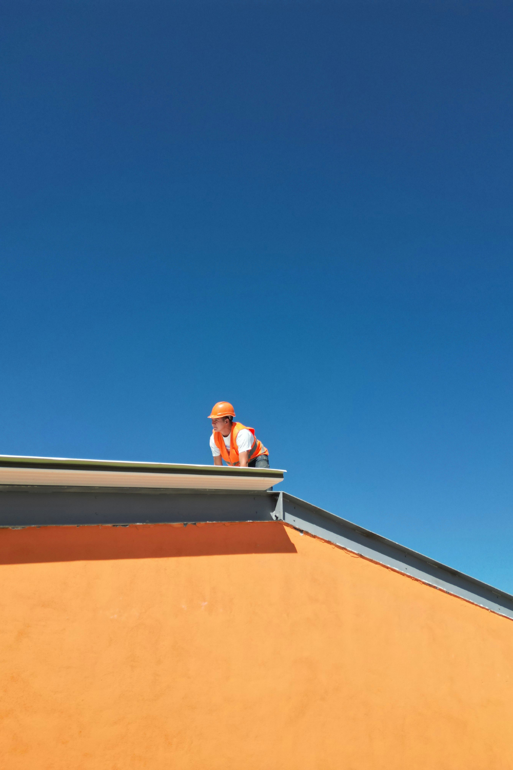 Construction worker in orange vest and hat works on the roof of an orange house