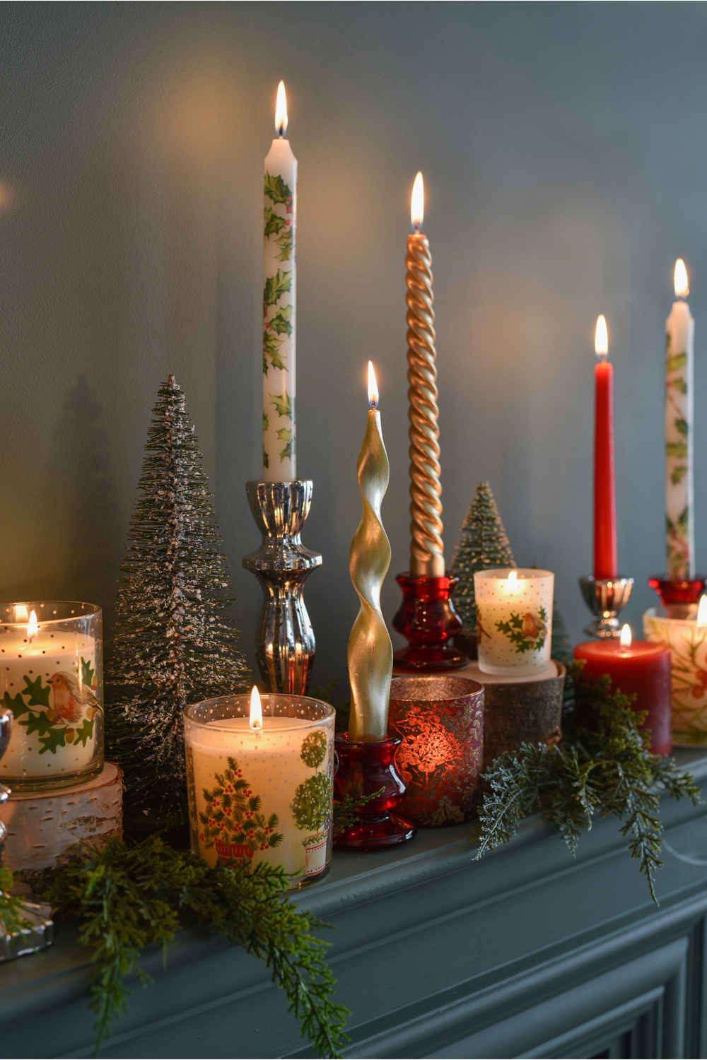 Row of red and gold candlesticks, and white jar candles on dark blue mantelpiece