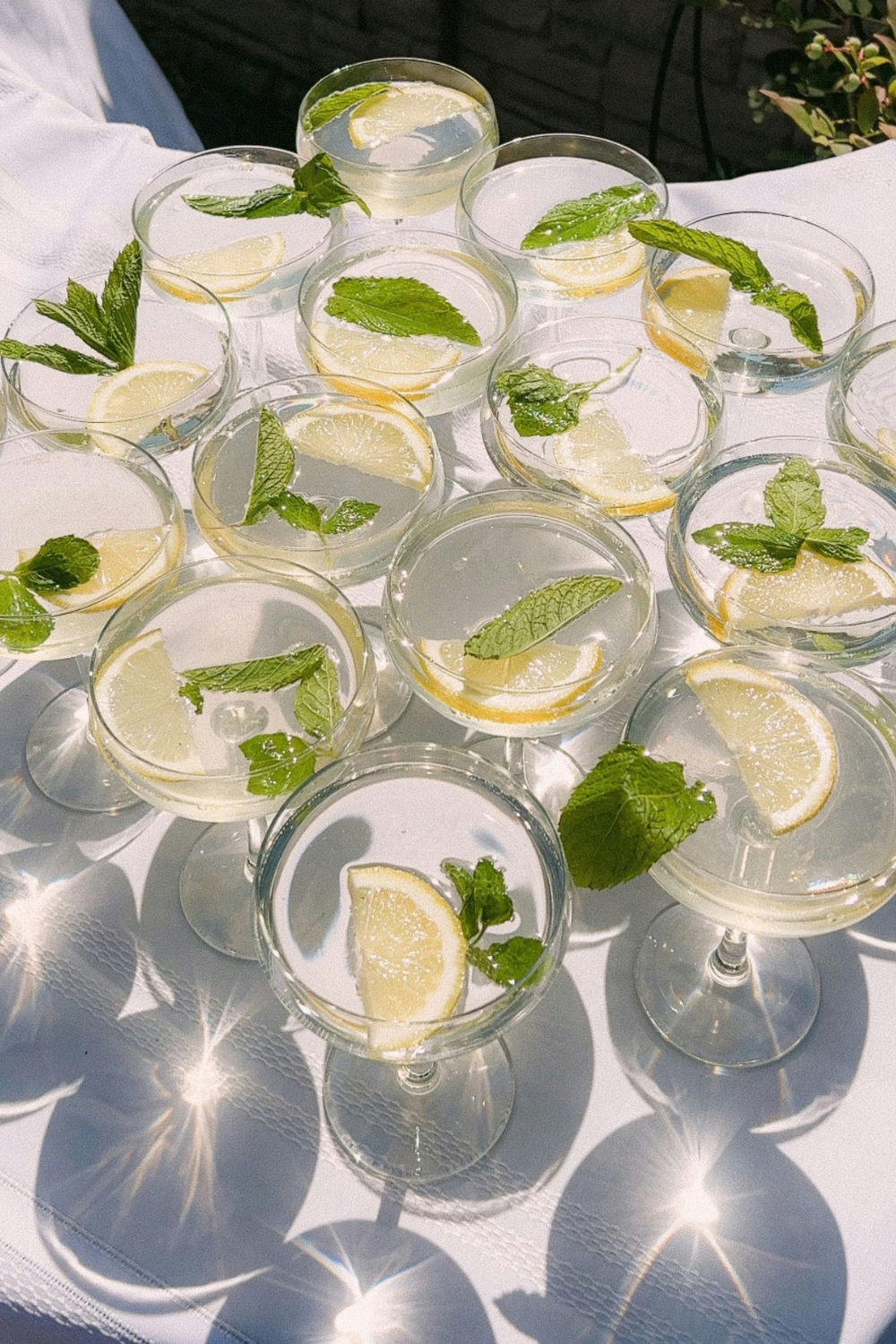 Cocktail glasses with mint and lemon on white tablecloth in the sun