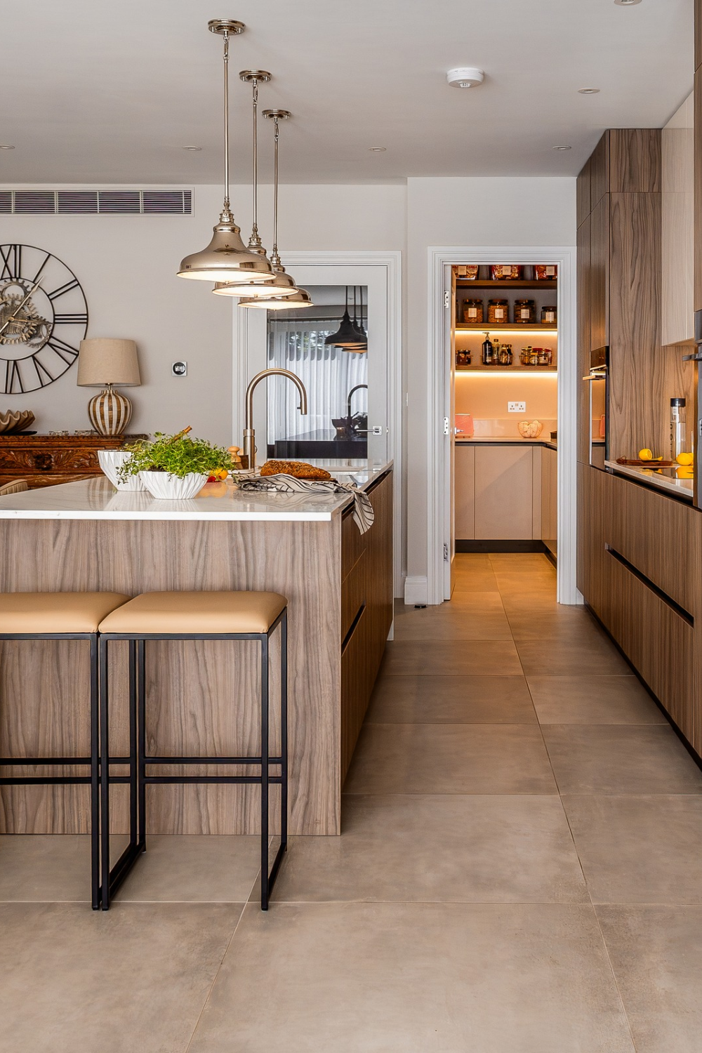Kitchen with wooden cabinets, island, gold hanging lamps and black bar stools