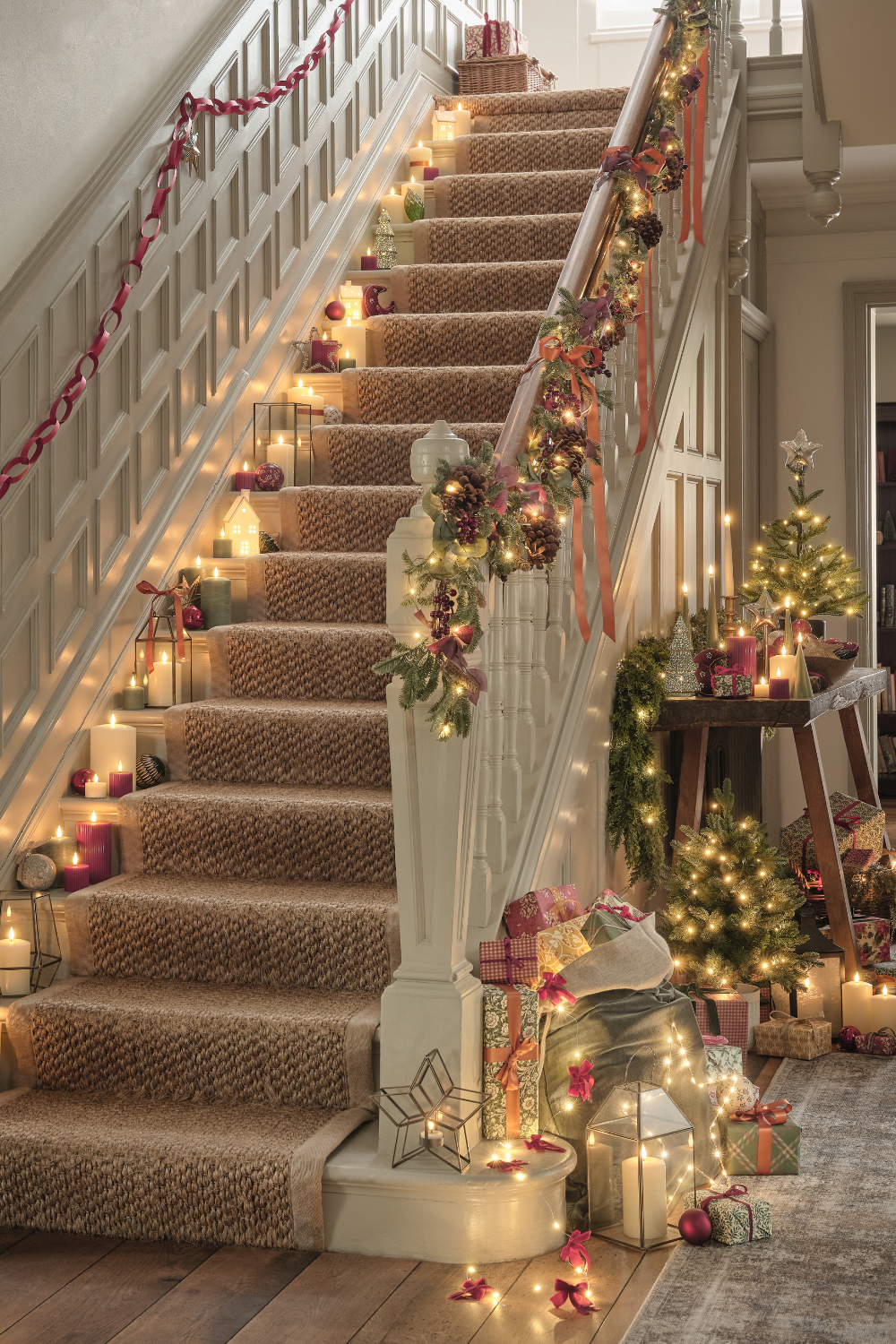 White staircase with wooden panelling and Christmas foliage garlands, candles and presents