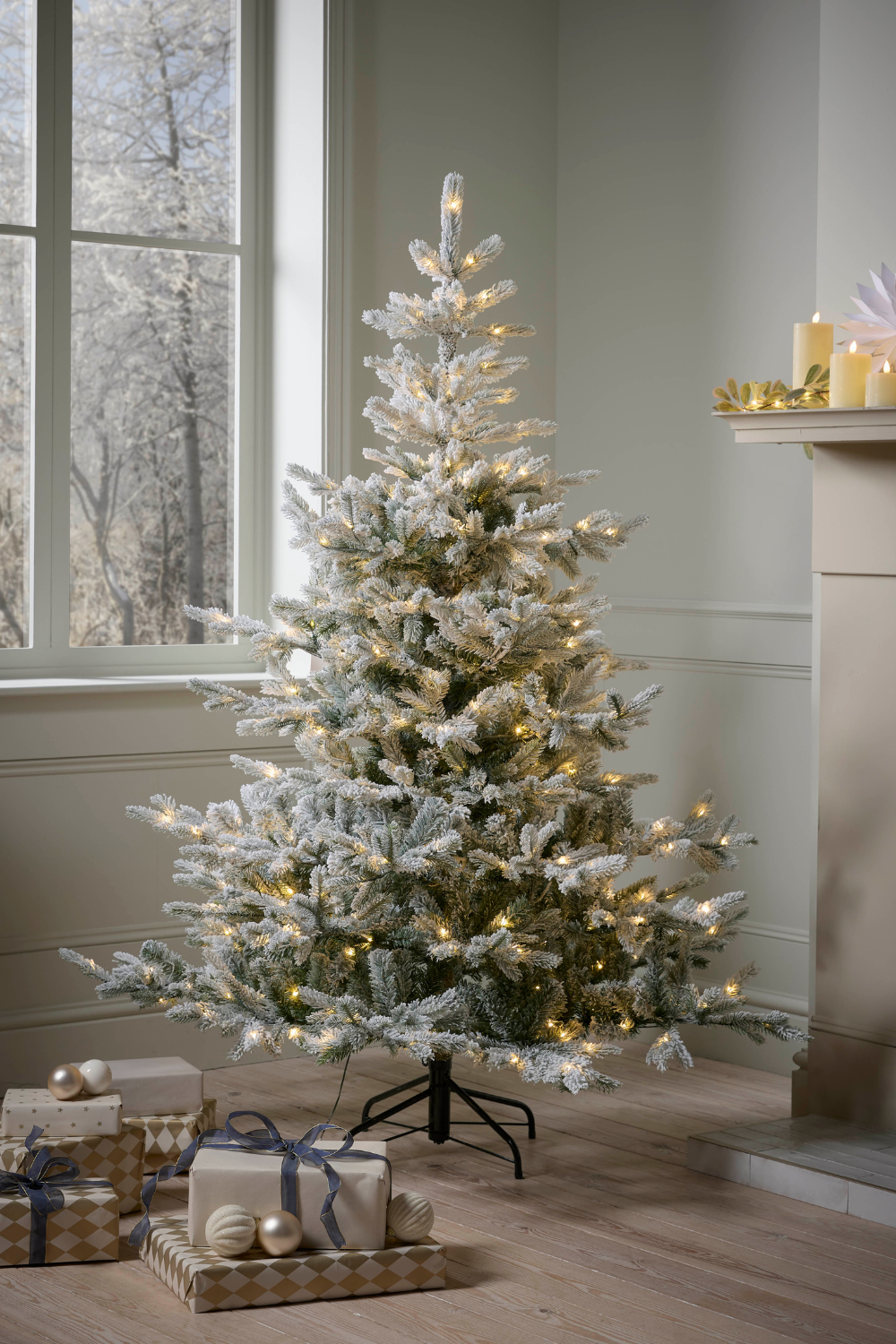 White Christmas tree with white & gold presents underneath next to mantelpiece with white candles